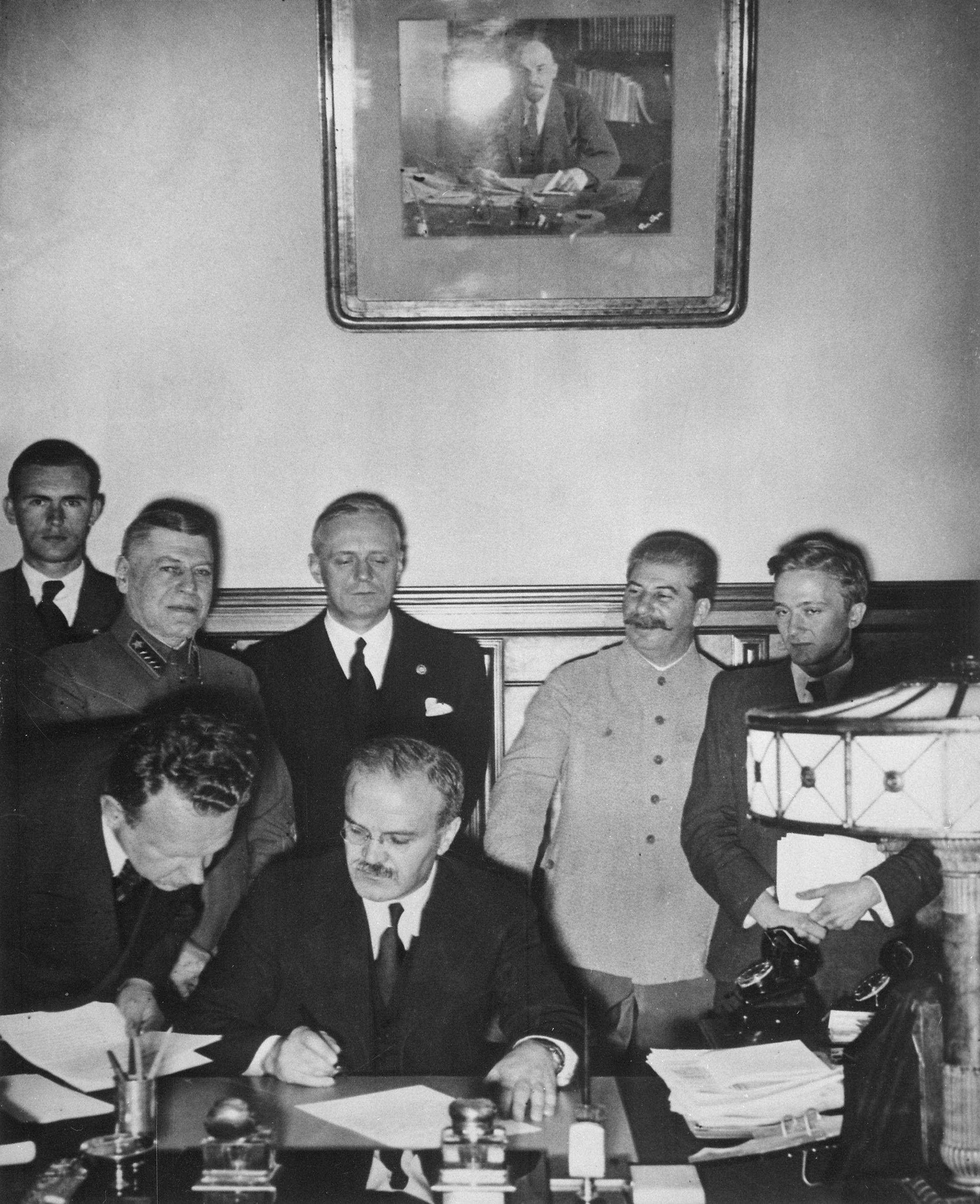 Ο Μόλοτοφ (υπογράφοντας), ο Ρίμπεντροπ (με τα μαύρα πίσω από τον Μόλοτοφ) και ο Στάλιν (δεξιά) στις 23 Αυγούστου 1939.